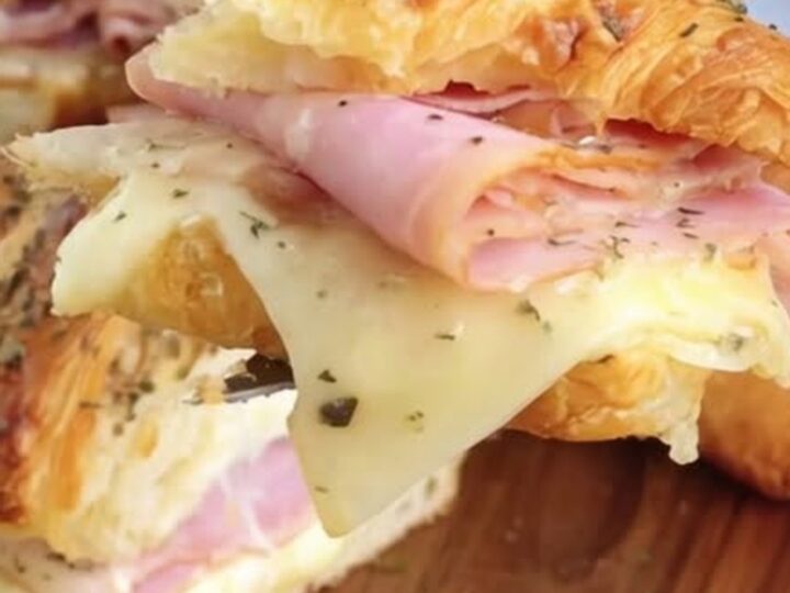 A warm, buttery croissant sandwich filled with layers of ham and melted Swiss cheese, held up for a close-up.