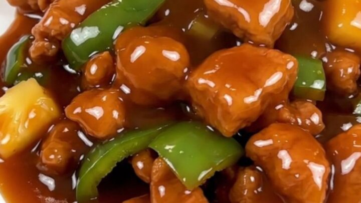 A close-up of glossy sweet and sour pork cubes with pineapple and green peppers in a slow cooker.