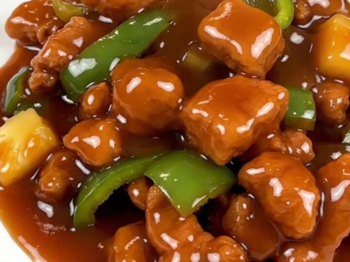 A close-up of glossy sweet and sour pork cubes with pineapple and green peppers in a slow cooker.