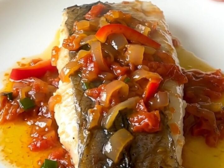 A plate of tender white hake fillets topped with a colorful piperade sauce of red peppers and onions.