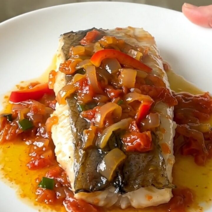 A plate of tender white hake fillets topped with a colorful piperade sauce of red peppers and onions.