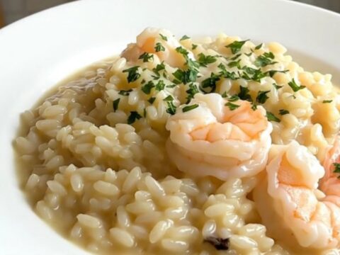 A top-down view of a black slow cooker filled with creamy seafood risotto on a quartz countertop.