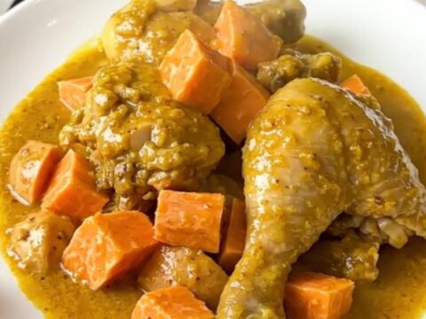 A top-down view of chicken thighs and cubed sweet potatoes in a slow cooker, seasoned with yellow colombo powder.
