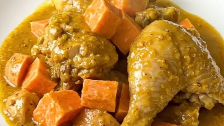 A top-down view of chicken thighs and cubed sweet potatoes in a slow cooker, seasoned with yellow colombo powder.