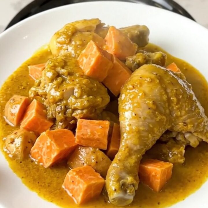 A top-down view of chicken thighs and cubed sweet potatoes in a slow cooker, seasoned with yellow colombo powder.