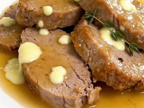 A close-up of sliced pork tenderloin on a white plate covered in a creamy goat cheese sauce.