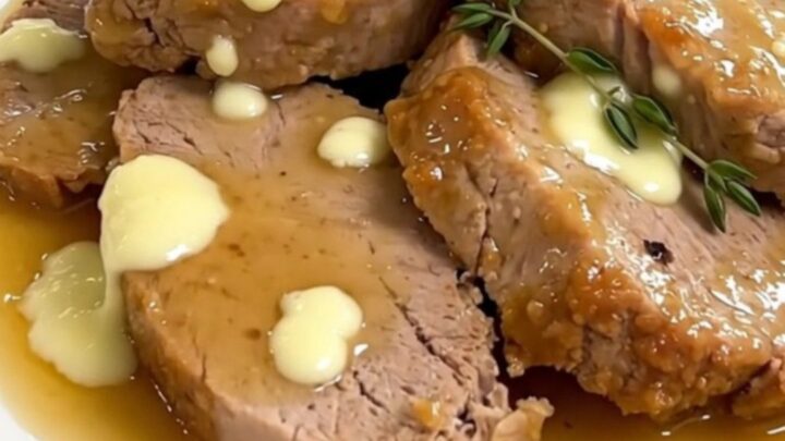 A close-up of sliced pork tenderloin on a white plate covered in a creamy goat cheese sauce.