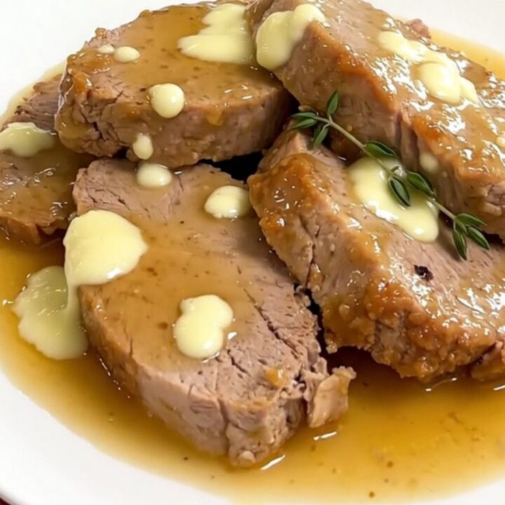 A close-up of sliced pork tenderloin on a white plate covered in a creamy goat cheese sauce.