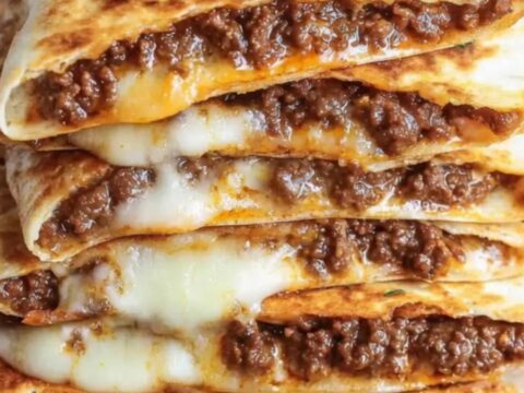 A stack of golden-brown, crispy ground beef quesadilla wedges on a wooden board.
