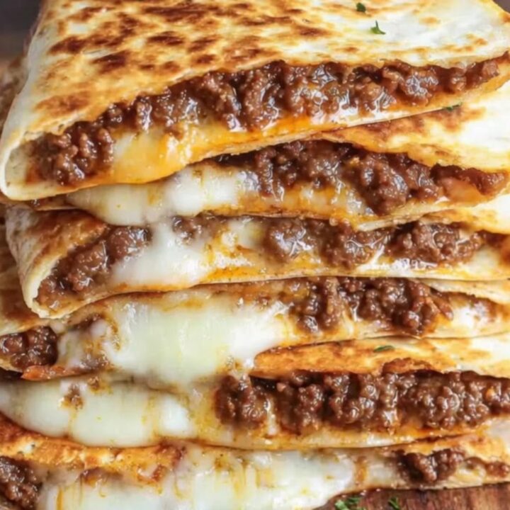 A stack of golden-brown, crispy ground beef quesadilla wedges on a wooden board.