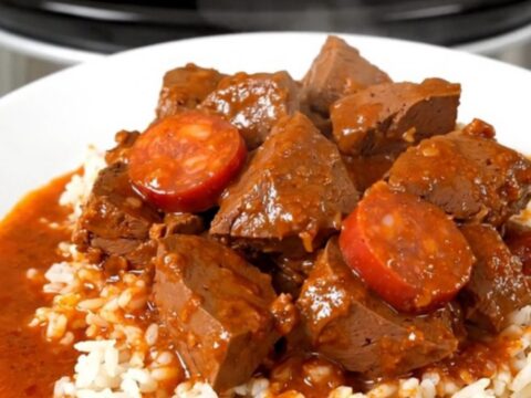 A hearty bowl of veal and chorizo stew served over white rice on a clean, white plate.