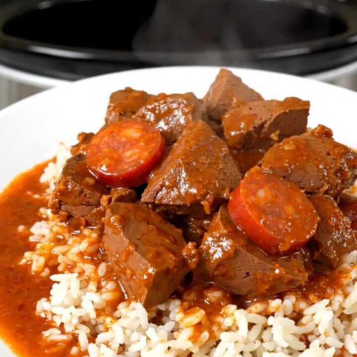 A hearty bowl of veal and chorizo stew served over white rice on a clean, white plate.