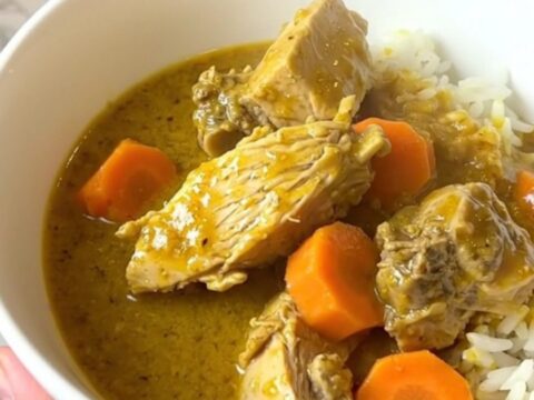 A steaming, glossy bowl of turkey curry with carrots served over white rice.
