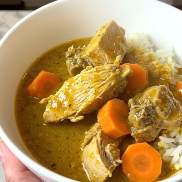A steaming, glossy bowl of turkey curry with carrots served over white rice.