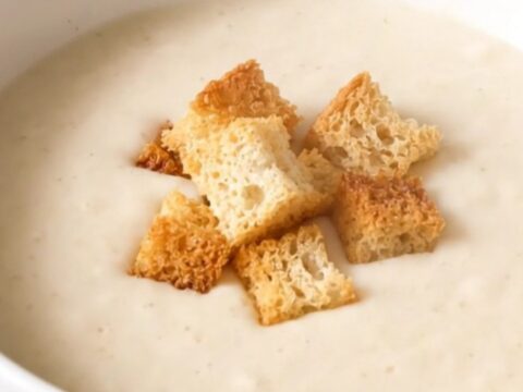 A white bowl filled with creamy white cauliflower velouté, garnished with golden croutons.