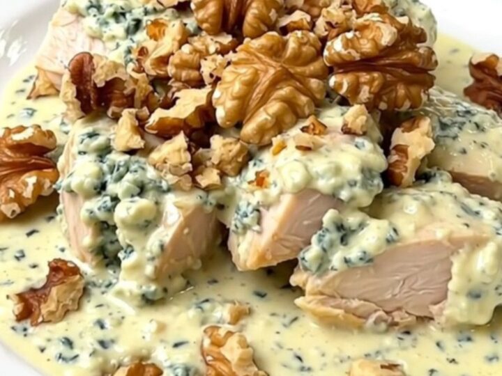 A top-down view of a slow cooker filled with raw chicken breasts, crumbled Roquefort, and crème fraîche.