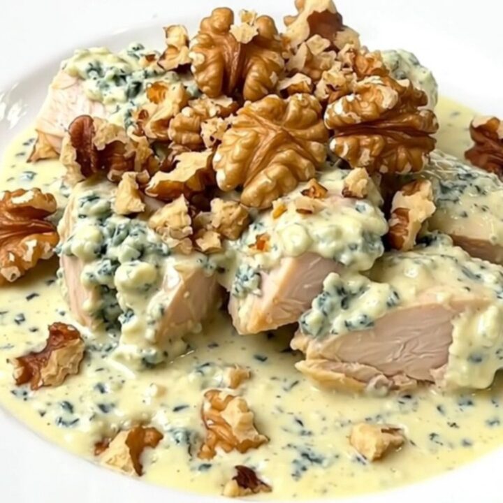 A top-down view of a slow cooker filled with raw chicken breasts, crumbled Roquefort, and crème fraîche.