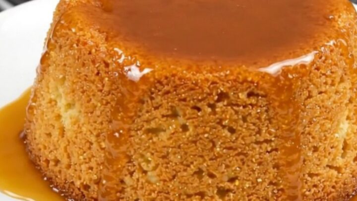 A close-up view of a golden semolina pudding cake with caramel drizzle on a white plate.