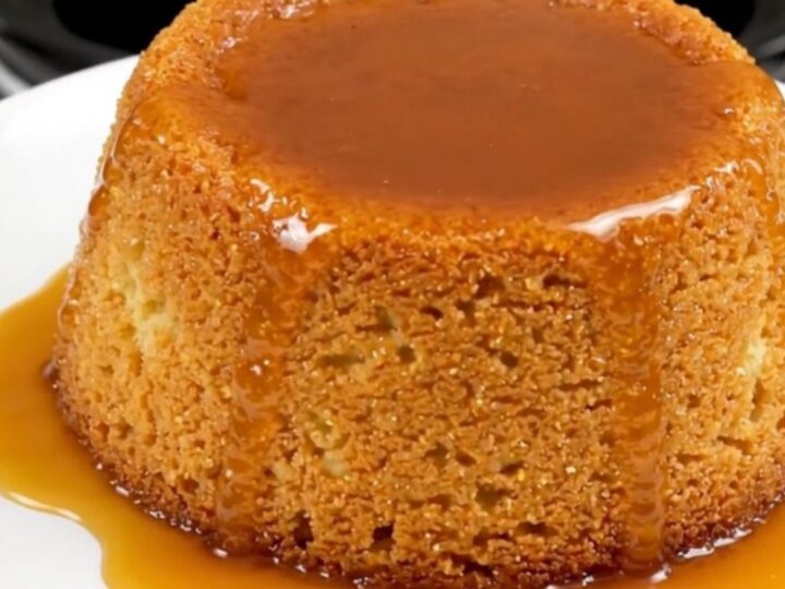 A close-up view of a golden semolina pudding cake with caramel drizzle on a white plate.