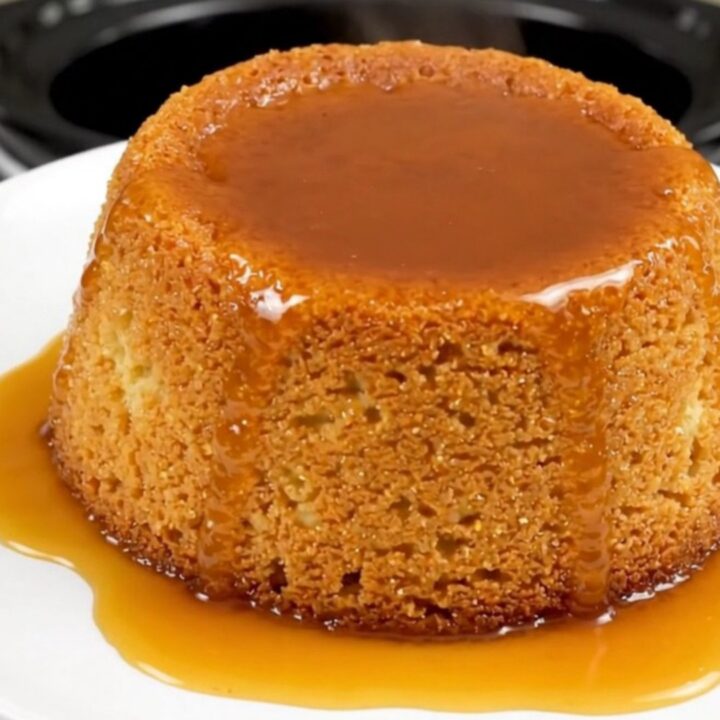 A close-up view of a golden semolina pudding cake with caramel drizzle on a white plate.