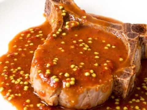 A steaming, tender pork chop coated in a rich, glossy charcutière sauce on a white plate.