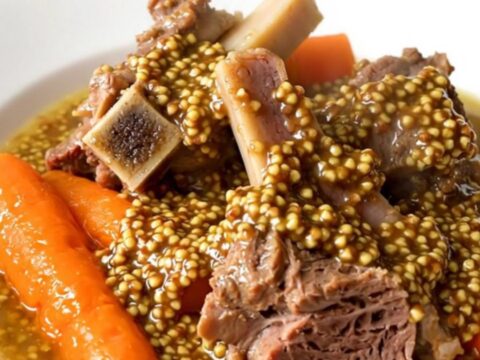 A close-up of a bowl of slow cooker lamb stew with visible carrots and mustard sauce.