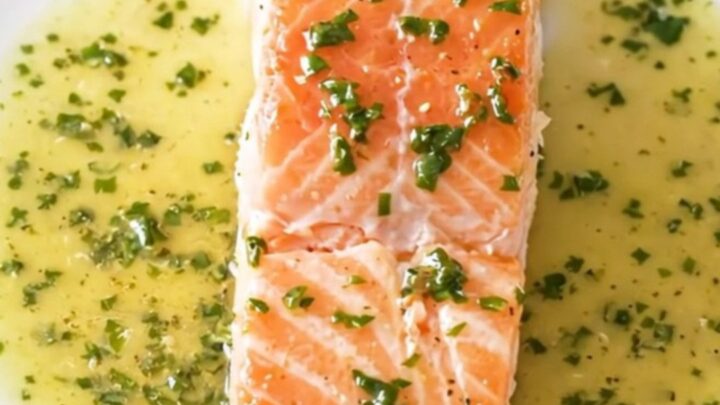 A close-up of a perfectly cooked salmon fillet covered in a creamy white wine and sorrel sauce.
