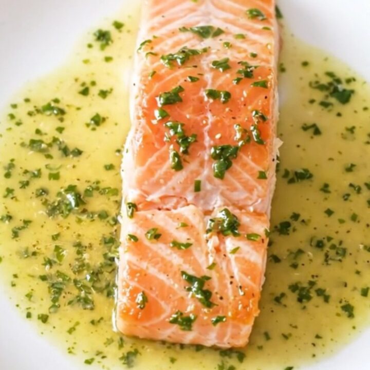 A close-up of a perfectly cooked salmon fillet covered in a creamy white wine and sorrel sauce.