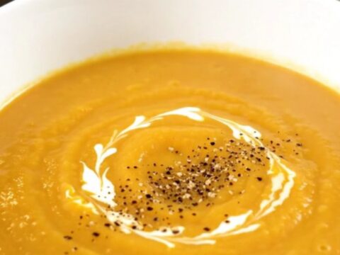 A bowl of silky, creamy turnip and carrot soup garnished with a swirl of cream and black pepper.