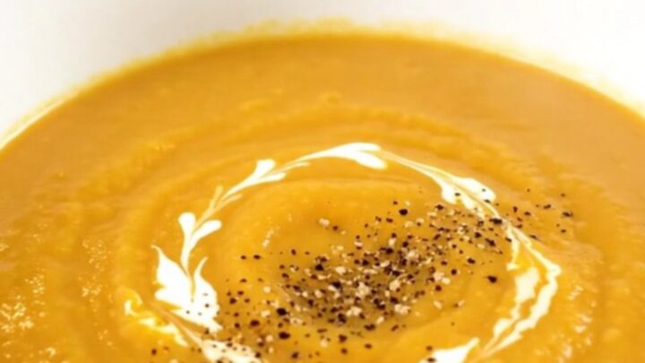 A bowl of silky, creamy turnip and carrot soup garnished with a swirl of cream and black pepper.