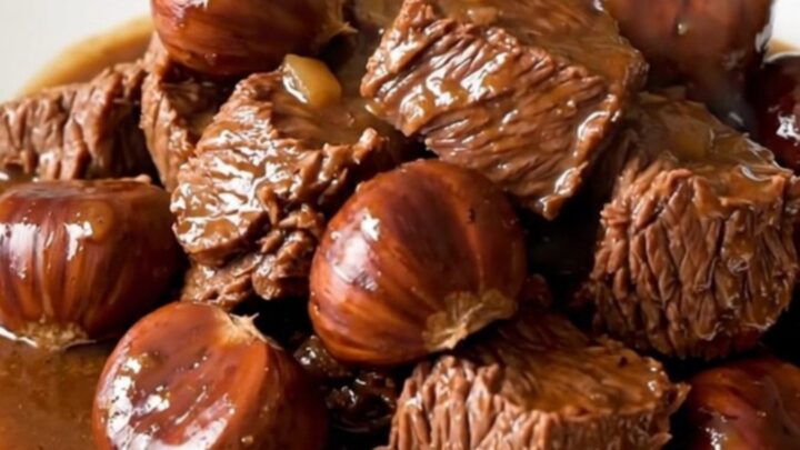 A close-up of a bowl filled with rich beef and chestnut stew, featuring glossy gravy and tender meat chunks.