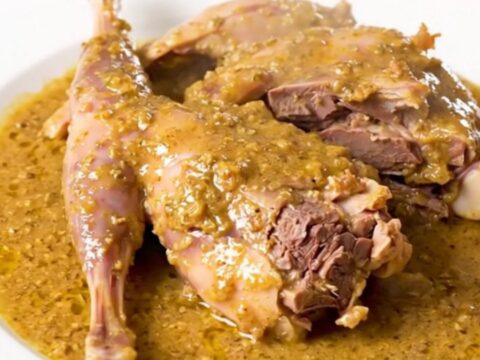 A slow cooker filled with rabbit pieces, shallots, and a white wine sauce.