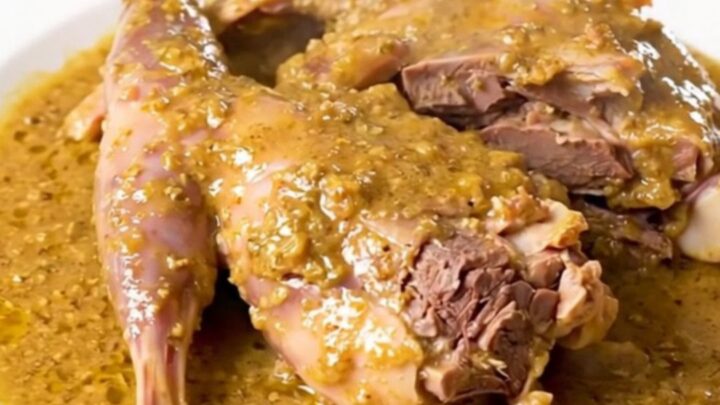 A slow cooker filled with rabbit pieces, shallots, and a white wine sauce.