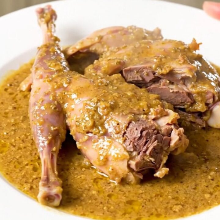 A slow cooker filled with rabbit pieces, shallots, and a white wine sauce.