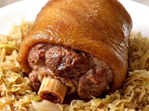 A glossy, tender pork shank nestled in a bed of warm sauerkraut on a white plate.