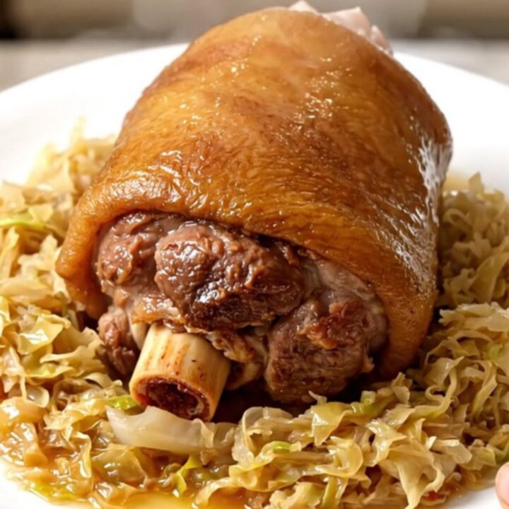 A glossy, tender pork shank nestled in a bed of warm sauerkraut on a white plate.