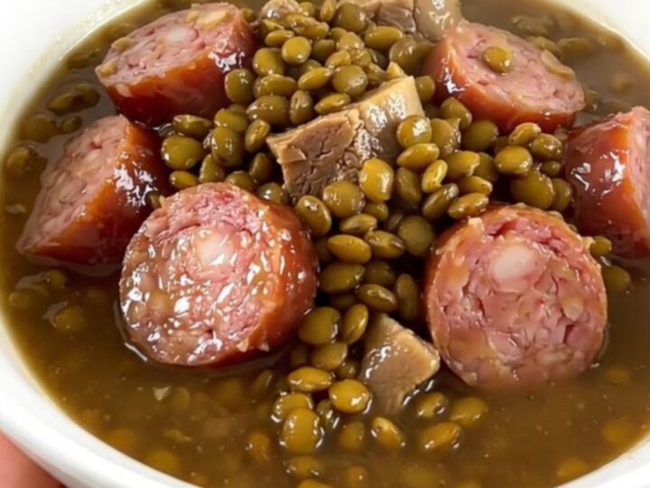 A rustic, steaming bowl of French potée berrichonne featuring lentils, sliced smoked sausage, and carrots.