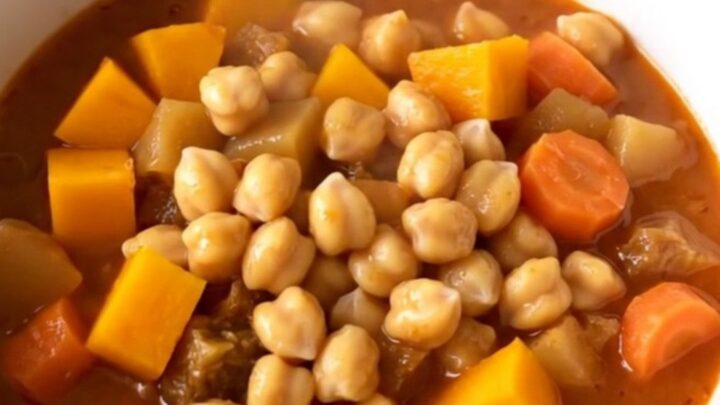 A close-up of a bowl filled with a vibrant chickpea and autumn vegetable stew featuring squash and carrots.