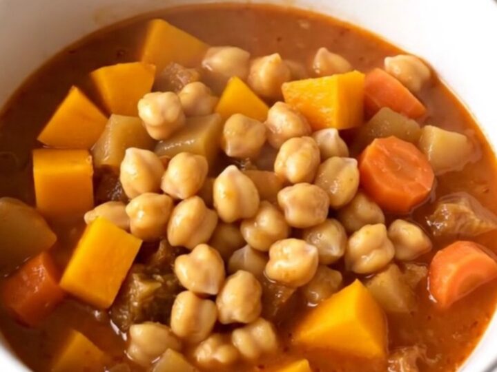 A close-up of a bowl filled with a vibrant chickpea and autumn vegetable stew featuring squash and carrots.