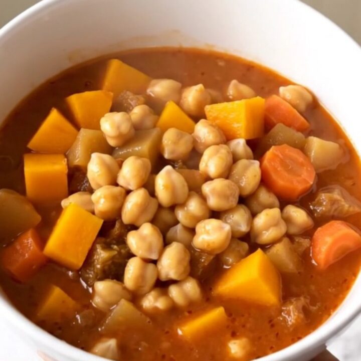 A close-up of a bowl filled with a vibrant chickpea and autumn vegetable stew featuring squash and carrots.