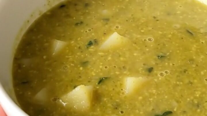 A steaming, glossy bowl of vibrant green spinach and potato soup held by a hand in a bright kitchen.