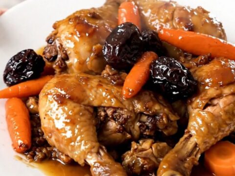 A close-up of tender, glazed chicken thighs with sliced carrots and prunes in a slow cooker.