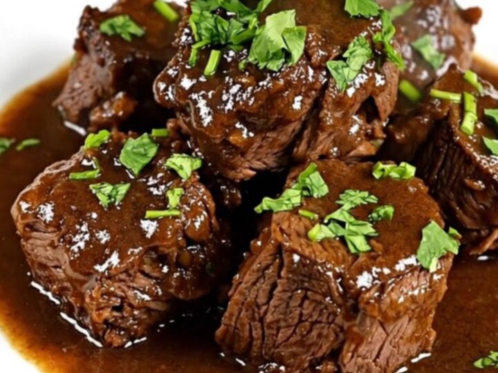 A close-up of a white ceramic plate filled with tender beef cubes, carrots, and mushrooms in a glossy white wine sauce.