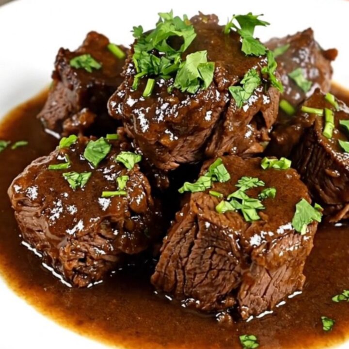 A close-up of a white ceramic plate filled with tender beef cubes, carrots, and mushrooms in a glossy white wine sauce.