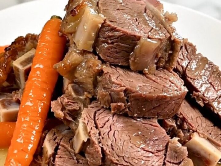 A slow-cooked boneless leg of lamb served on a white plate with tender carrots and shallots, glistening with pan juices.