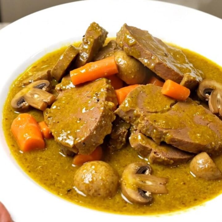 A close-up of a steaming bowl of coconut curry veal blanquette topped with fresh herbs.