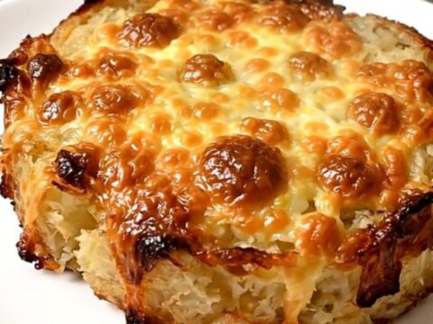 A top-down view of a black slow cooker filled with layered sliced potatoes, cheese, and broth.