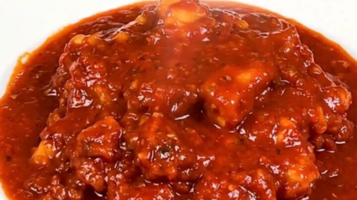 A close-up of a steaming, glossy cod rougail served on a white plate with a rich tomato sauce.
