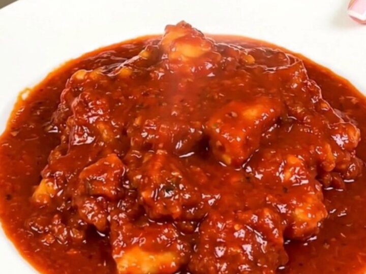 A close-up of a steaming, glossy cod rougail served on a white plate with a rich tomato sauce.