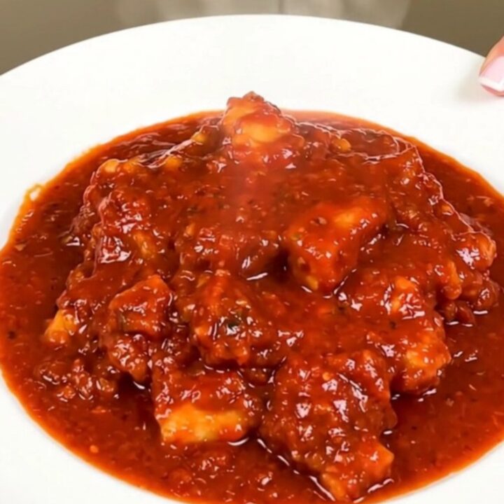 A close-up of a steaming, glossy cod rougail served on a white plate with a rich tomato sauce.